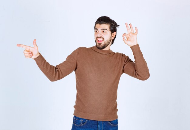 Imagen de un joven modelo sonriente de pie y apuntando hacia otro lado con el dedo índice. Foto de alta calidad