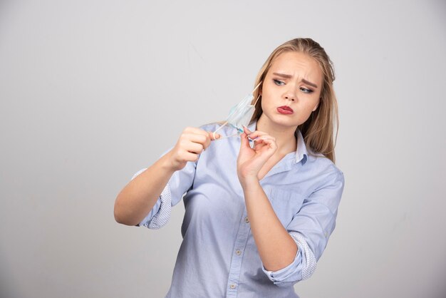 Imagen de una joven mujer bonita de pie y quitándose una máscara médica