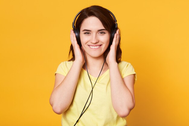 Imagen de la joven mujer feliz con auriculares escuchando música aislada sobre amarillo