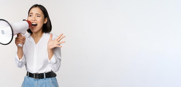 Imagen de una joven reclutadora activista coreana gritando en megáfono buscando gritando en el altavoz de pie sobre fondo blanco.