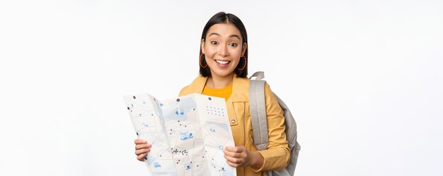 Imagen de una joven turista asiática con mapa y mochila posando sobre fondo blanco de estudio