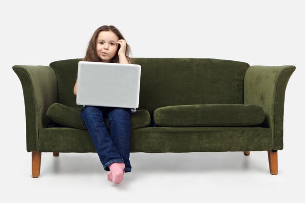 Imagen de una linda chica pensativa usando la computadora portátil mientras hace la tarea, rascándose la cabeza, con mirada dudosa e incierta