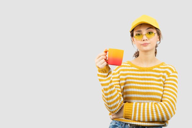 Imagen de linda mujer joven en vasos de pie y sosteniendo una taza. Foto de alta calidad