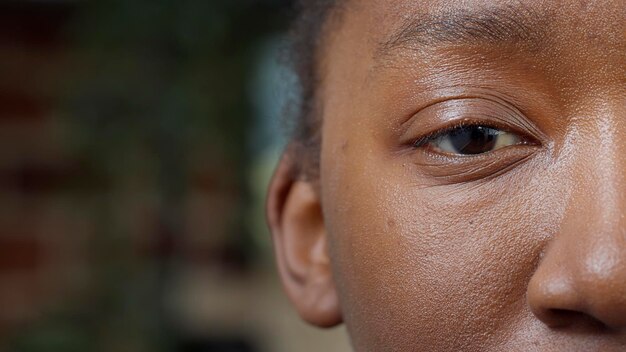 Imagen macro de un adulto joven sonriendo y mirando a la cámara, mostrando un ojo y la mitad de la cara. Modelo femenino que enfoca la vista, tiene pestañas, cejas, pupila, retina e iris. De cerca.