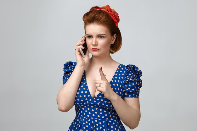 Imagen de madre joven enojada en traje vintage con aspecto estricto, levantando el dedo índice frente a ella como señal de advertencia