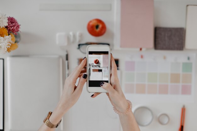 Imagen de manos femeninas tomando retratos de escritorio con papelería, gafas y apple en smartphone