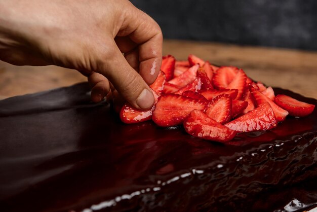 Imagen de manos poniendo fresas en tarta de chocolate.