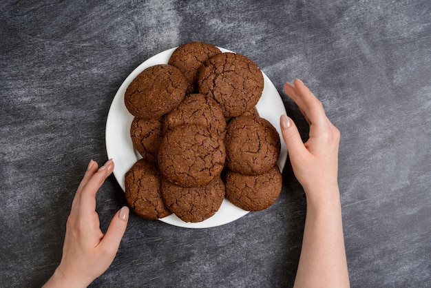 Imagen de manos sosteniendo galletas de chocolate sobre superficie de madera