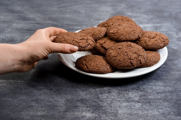 Imagen de manos sostienen galletas de chocolate en un plato