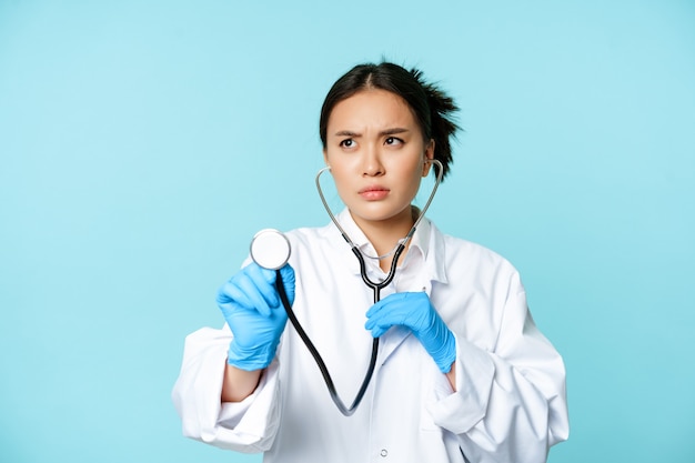 Imagen del médico asiático serio del trabajador médico que escucha los pulmones del paciente con el estetoscopio que examina p ...