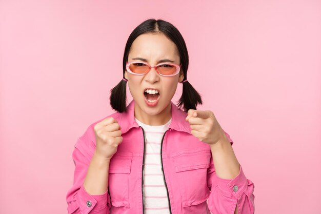 Imagen de una modelo adulta coreana enojada y cabreada agitando los puños y gritando indignada de pie sobre un fondo rosa