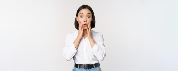 Imagen de una modelo asiática que parece sorprendida mirando asombrada reaccionando ante las grandes noticias sorpresa de pie sobre fondo blanco