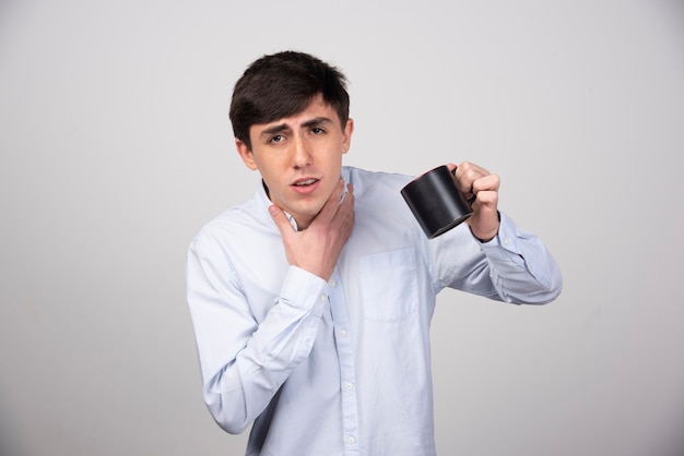 Imagen de un modelo de chico confundido de pie con una taza y mirando a la cámara