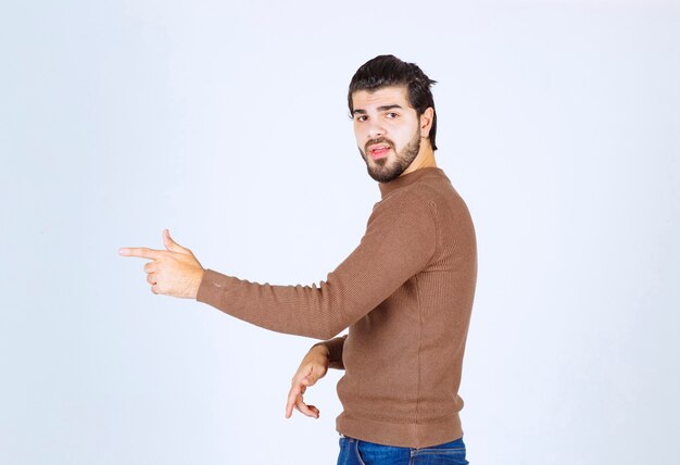 Imagen de un modelo de hombre guapo joven de pie y apuntando hacia afuera. Foto de alta calidad