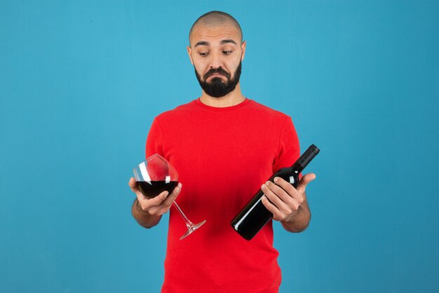 Imagen de un modelo de hombre joven en t-short rojo sosteniendo una botella de vino con vidrio.