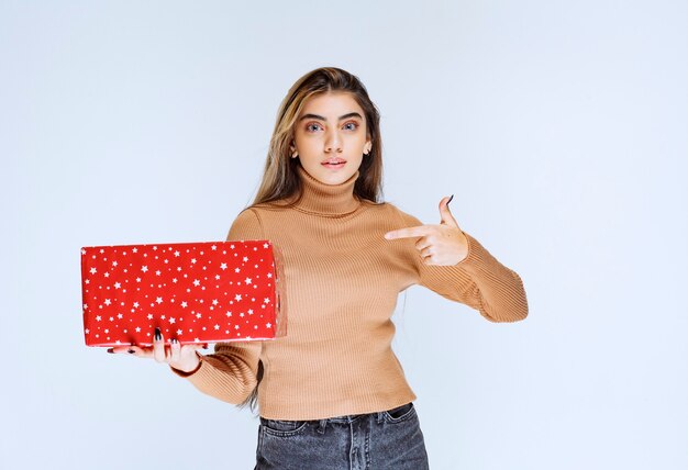 Imagen de un modelo de mujer atractiva apuntando a un presente rojo.