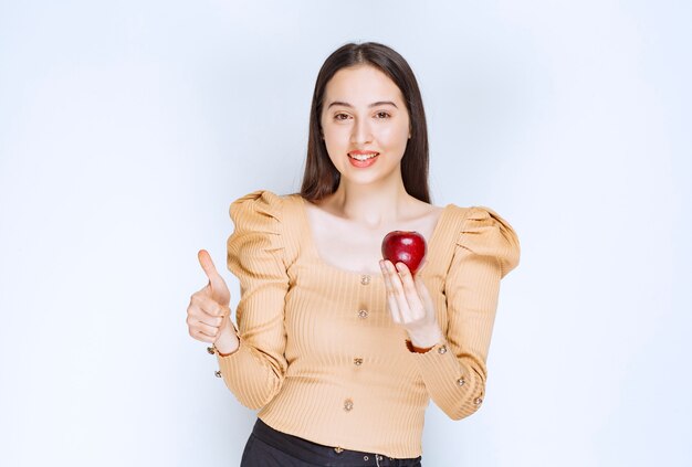 Imagen de un modelo de mujer bonita sosteniendo una manzana roja fresca y mostrando un pulgar hacia arriba.