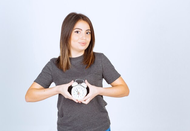 Imagen de un modelo de mujer joven y agradable que muestra un reloj despertador.