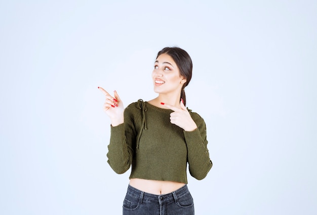 Imagen de un modelo de mujer joven de pie y apuntando a un lado con el dedo índice