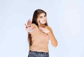 Foto gratuita imagen de un modelo de mujer joven en suéter marrón de pie y haciendo señal de stop.
