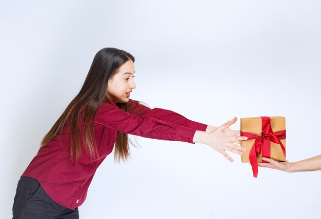 Imagen de un modelo de mujer joven tomando un regalo con lazo en una pared blanca.