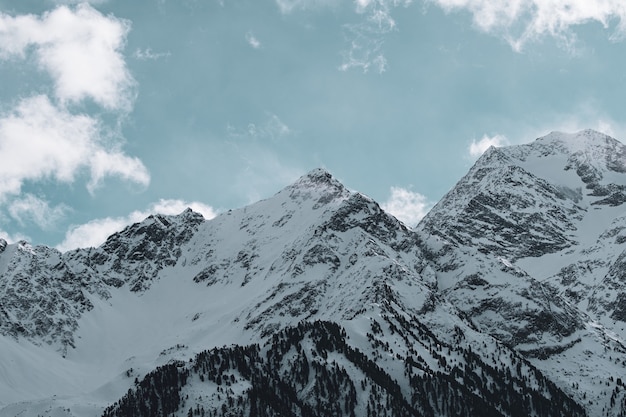 Imagen de montañas rocosas cubiertas de nieve bajo un cielo nublado y la luz del sol