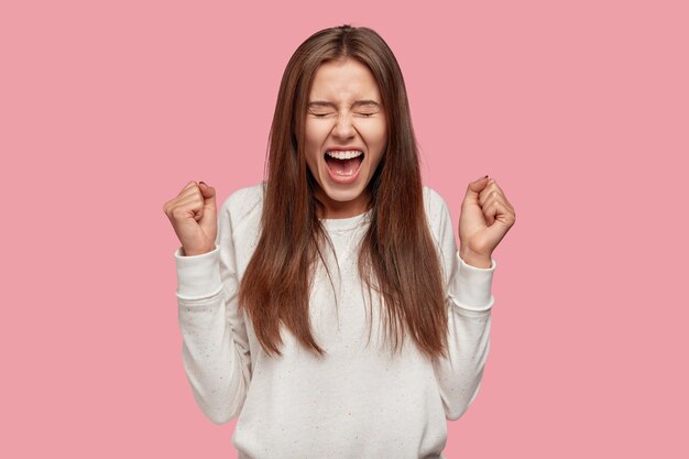 Imagen de morena asombrada adolescente aprieta los puños con triunfo y éxito, gestos interiores, exclama con felicidad