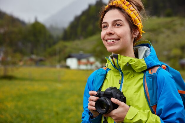 Imagen de mujer alegre de aspecto agradable vestida informalmente, tiene cámara profesional