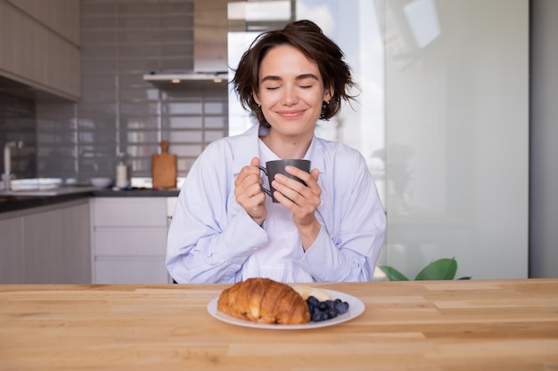 Imagen de una mujer alegre sonriendo con los ojos cerrados sosteniendo una taza