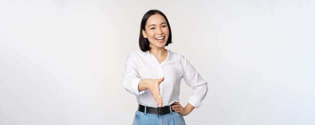 Imagen de una mujer asiática confiada sonriendo extendiendo la mano para un gesto de saludo de apretón de manos diciendo hola de pie sobre fondo blanco