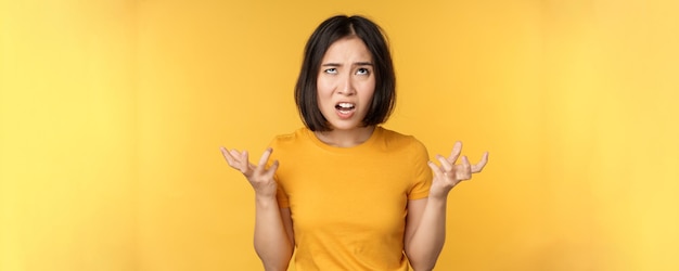 Imagen de una mujer asiática enojada gritando y maldiciendo con una expresión indignada y furiosa sobre un fondo amarillo