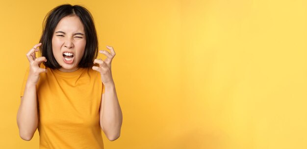 Imagen de una mujer asiática enojada gritando y maldiciendo mirando indignada expresión de la cara furiosa de pie ov