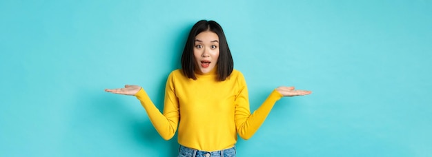 Foto gratuita imagen de una mujer asiática indecisa encogiéndose de hombros extendiendo las manos hacia los lados y mirando despistada a ca