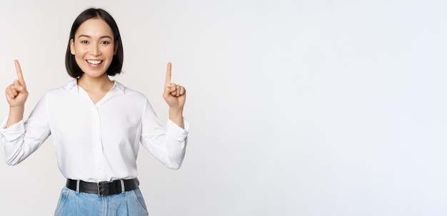 Imagen de una mujer asiática sonriente y segura de sí misma señalando con el dedo hacia arriba mostrando un banner o información de venta