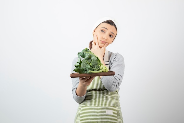 Foto gratuita imagen de una mujer atractiva pensativa sosteniendo un plato de madera de brócoli