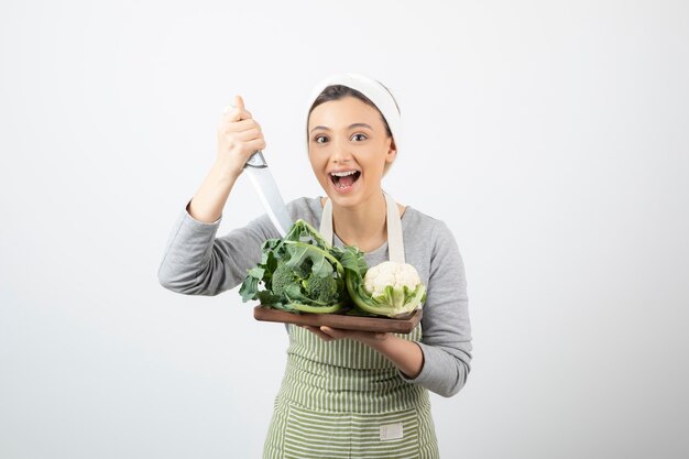 Imagen de una mujer atractiva sonriente sosteniendo un cuchillo con una placa de madera de coliflores