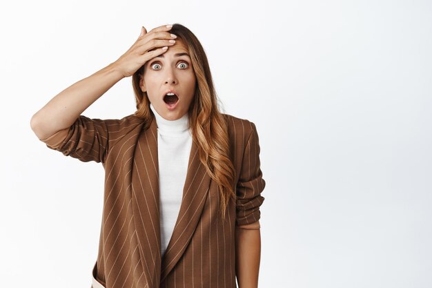 Imagen de una mujer corporativa mirando sorprendida a la cámara golpeándose la frente y mirando sorprendida con la mandíbula caída del fondo blanco de las grandes noticias