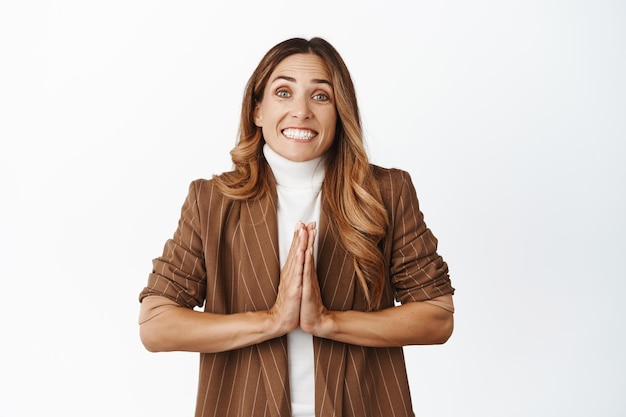 Imagen de una mujer corporativa sonriente pidiendo ayuda rogando con una expresión de cara linda y esperanzada, diga por favor de pie sobre fondo blanco