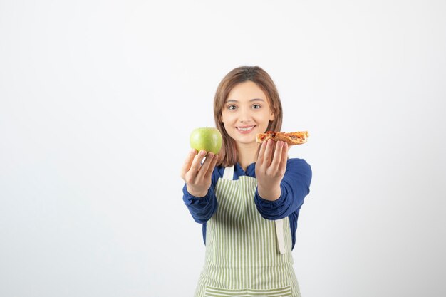 Imagen de mujer en delantal tratando de elegir qué comer manzana o pizza