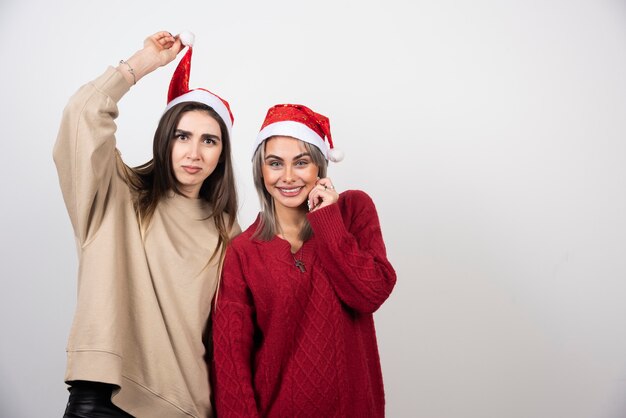 Imagen de una mujer feliz sosteniendo un gorro de Papá Noel cerca de su amiga bonita.