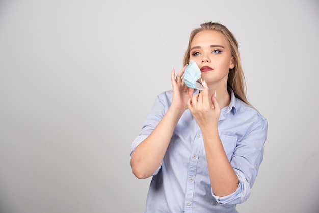 Imagen de una mujer guapa de pie y quitándose una mascarilla médica