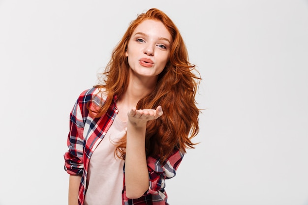 Imagen de mujer de jengibre complacida en camisa envía beso aéreo