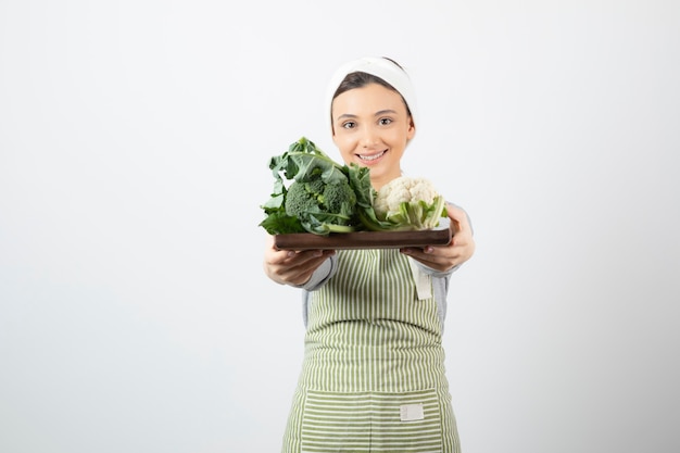 Foto gratuita imagen de una mujer joven y atractiva sosteniendo una placa de madera de coliflor y brócoli