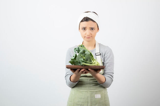 Imagen de una mujer joven y atractiva sosteniendo un plato de madera de brócoli
