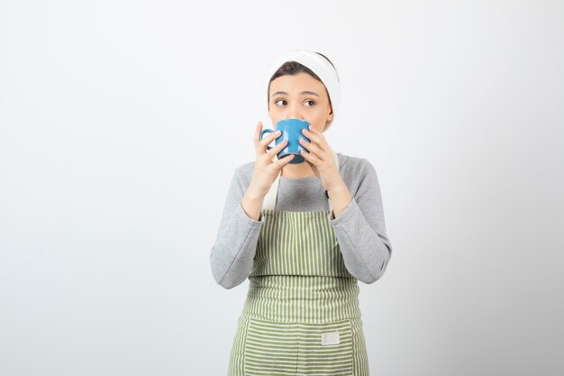 Imagen de una mujer joven y bonita en delantal bebiendo de una taza azul