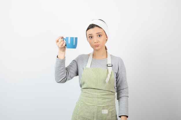 Imagen de una mujer joven y bonita en delantal sosteniendo una taza azul