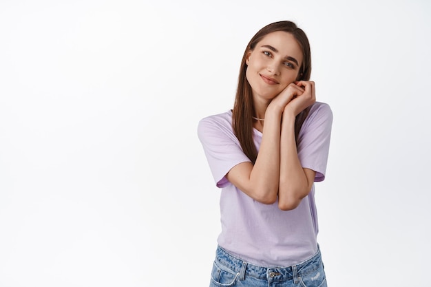 Imagen de una mujer joven mirando, contemplando algo hermoso y adorable, toma las manos cerca de la cara y suspira de admiración, de pie contra un fondo blanco