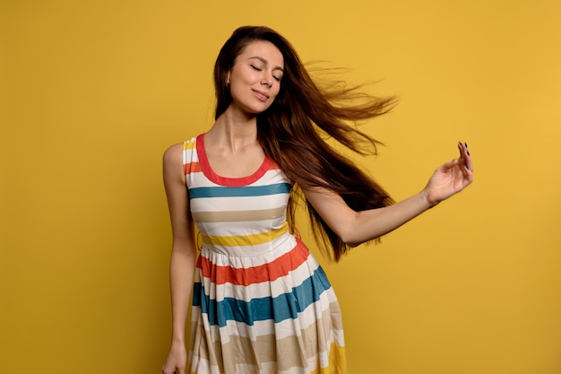 Imagen de una mujer joven muy sonriente en vestido de verano brillante aislada sobre pared amarilla. Retrato de moda de niña bonita posando divirtiéndose sobre pared colorida