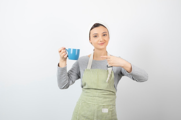 Imagen de una mujer joven sonriente en delantal apuntando a una taza azul