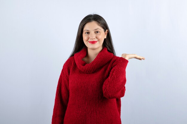 Imagen de una mujer joven en suéter rojo mostrando la mano sobre fondo blanco.
